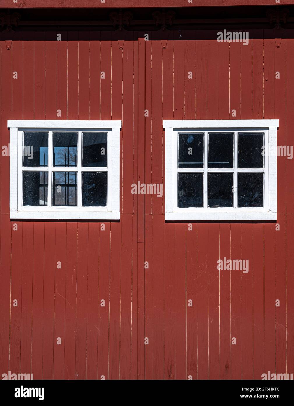 Foto einer Seite einer roten Scheune mit zwei weiß gerahmten Fenstern. Stockfoto