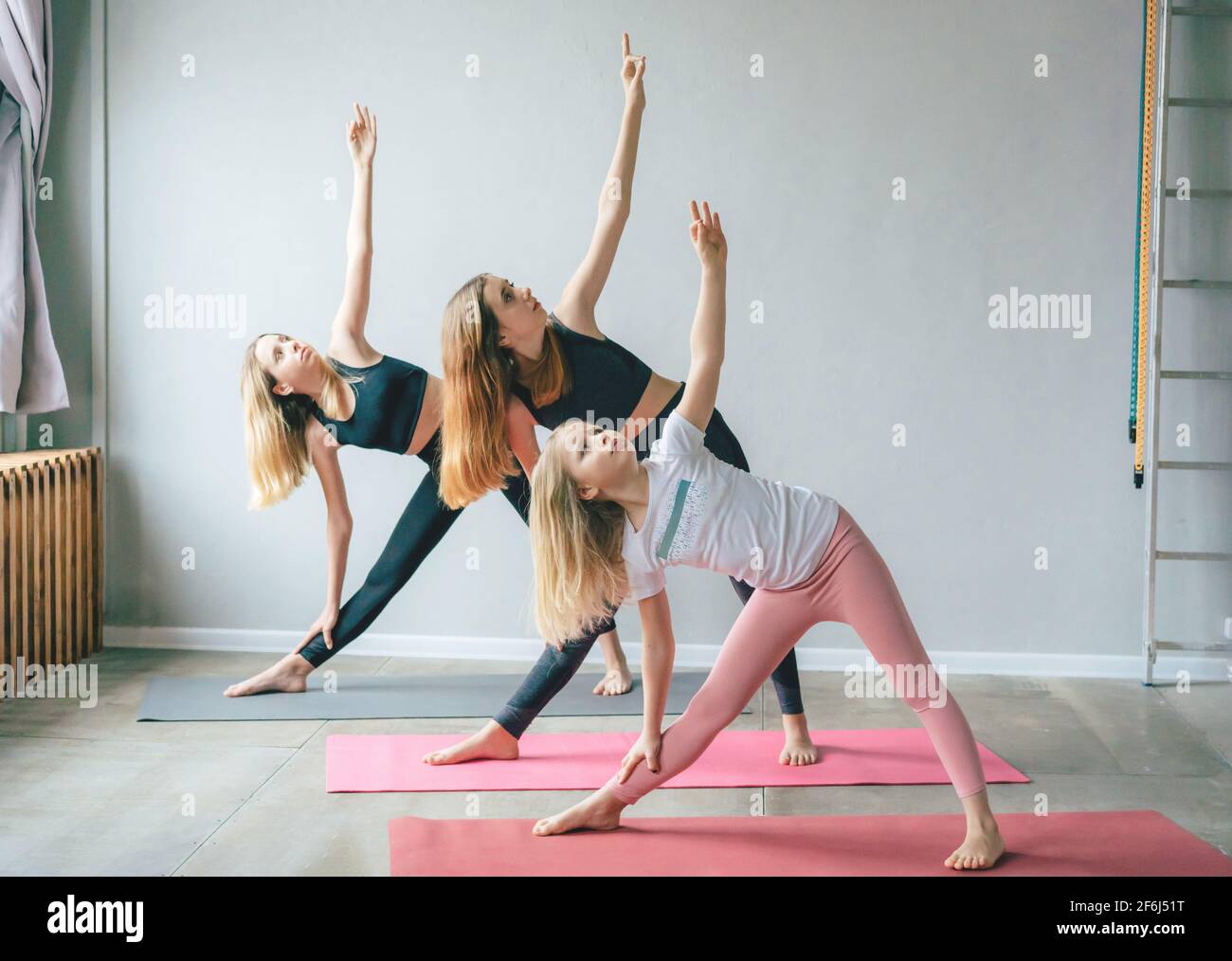 Drei weiße Teenager-Mädchen-Schwestern in Sport-Leggings stehen in einer Yoga-Pose auf den Matten im Fitnessstudio. Kümmern Sie sich um Ihren Körper, morgendliche Übungen und stre Stockfoto