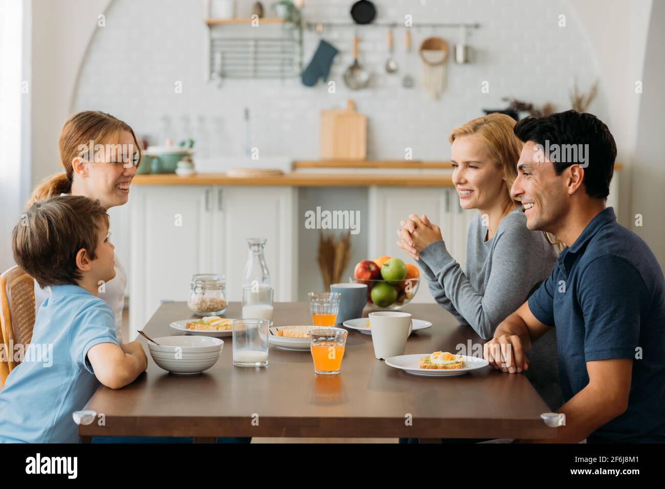 Lächelnde kaukasische Familie von Mann und Frau sitzen zusammen und Beim Essen dem kleinen und niedlichen Sohn mit Tochter zuhören Gesundes Frühstück zu Hause Stockfoto