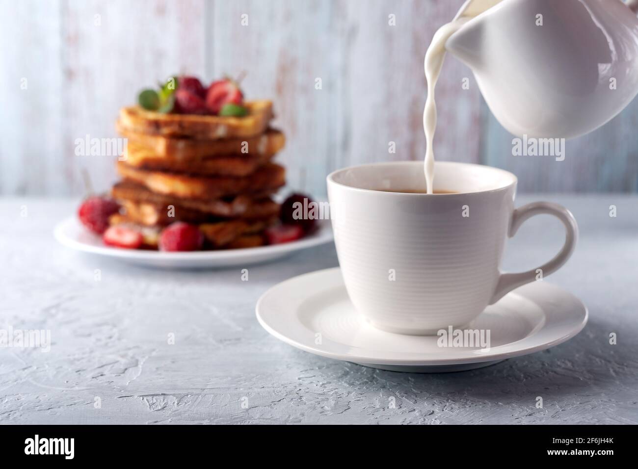 Eine Tasse Kaffee mit Rahm und French Toast mit Zimt und Erdbeeren. Frühstück am Morgen Stockfoto