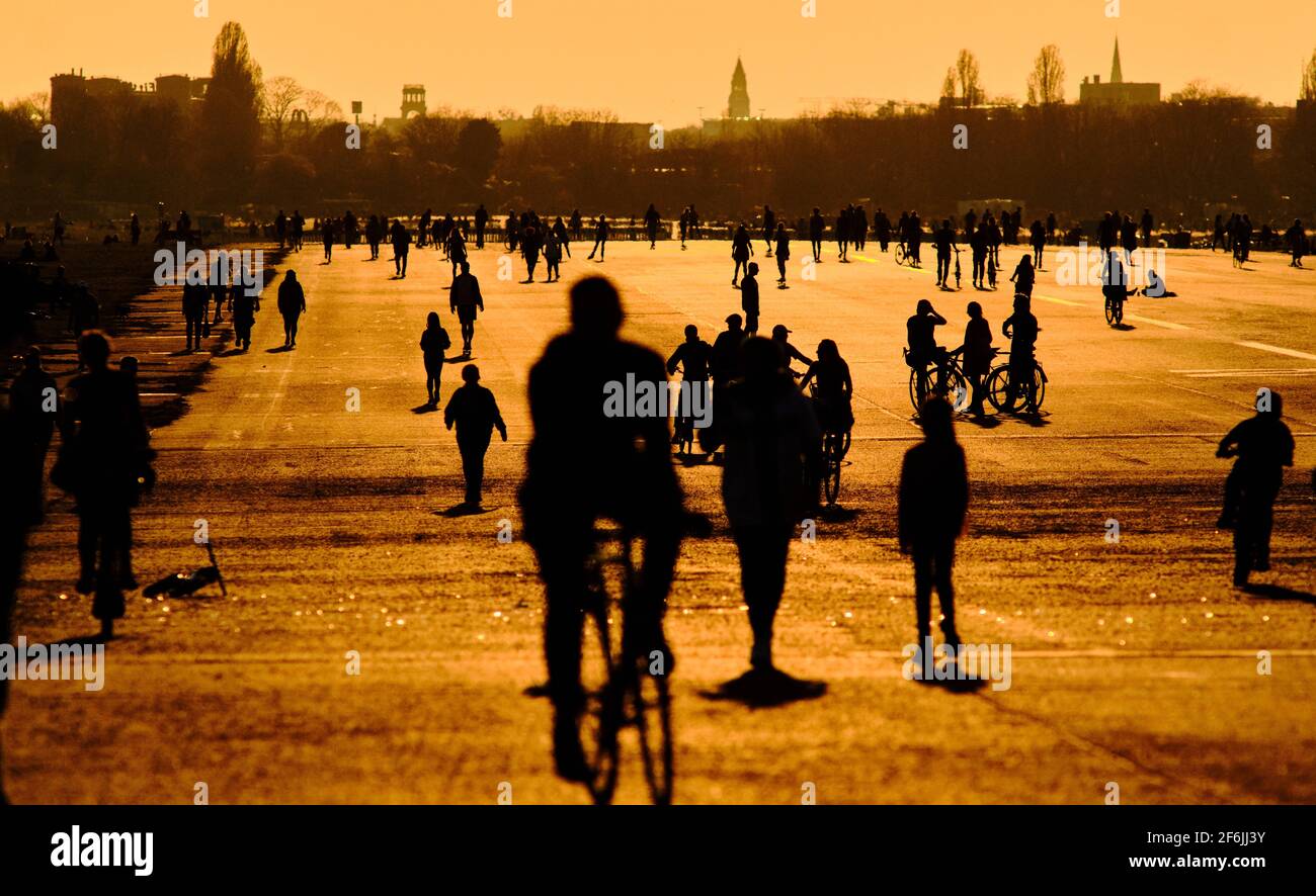 Berlin, Deutschland. März 2021. Im Licht der untergehenden Sonne laufen die Menschen über das Tempelhofer Feld. Die fast sommerlichen Temperaturen sorgten dafür, dass viele Menschen ihr Zuhause verließen, um Freunde und Bekannte zu treffen. Der Berliner Senat hat am Dienstag gegen eine Ausgangssperre entschieden und stattdessen strengere Kontaktbeschränkungen in den Abend- und Nachtstunden geplant. Beispielsweise könnte die Anzahl der Personen, die nachts an Meetings teilnehmen dürfen, auf zwei begrenzt werden, um Menschenmengen zu vermeiden. Quelle: Stefan Jaitner/dpa/Alamy Live News Stockfoto