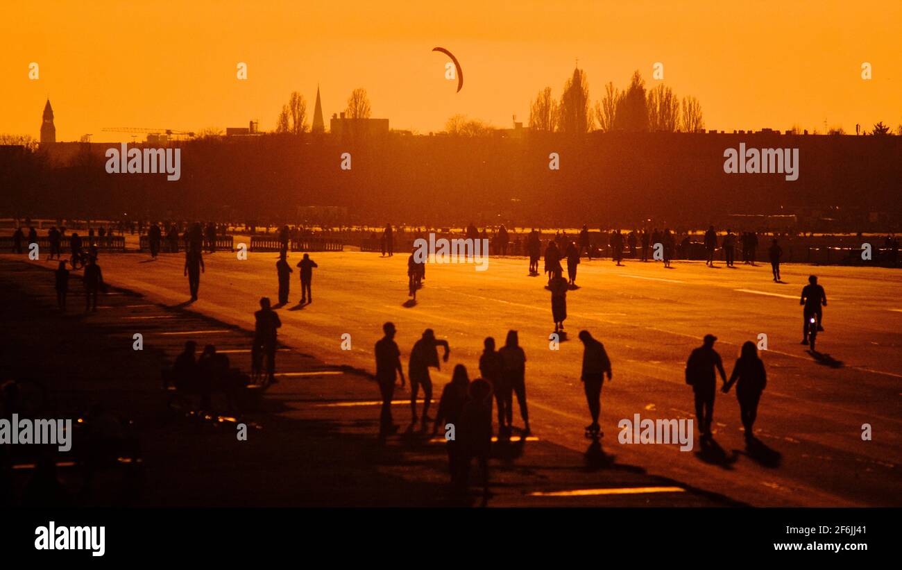 Berlin, Deutschland. März 2021. Im Licht der untergehenden Sonne laufen die Menschen über das Tempelhofer Feld. Die fast sommerlichen Temperaturen sorgten dafür, dass viele Menschen ihr Zuhause verließen, um Freunde und Bekannte zu treffen. Der Berliner Senat hat am Dienstag gegen eine Ausgangssperre entschieden und stattdessen strengere Kontaktbeschränkungen in den Abend- und Nachtstunden geplant. Beispielsweise könnte die Anzahl der Personen, die nachts an Meetings teilnehmen dürfen, auf zwei begrenzt werden, um Menschenmengen zu vermeiden. Quelle: Stefan Jaitner/dpa/Alamy Live News Stockfoto