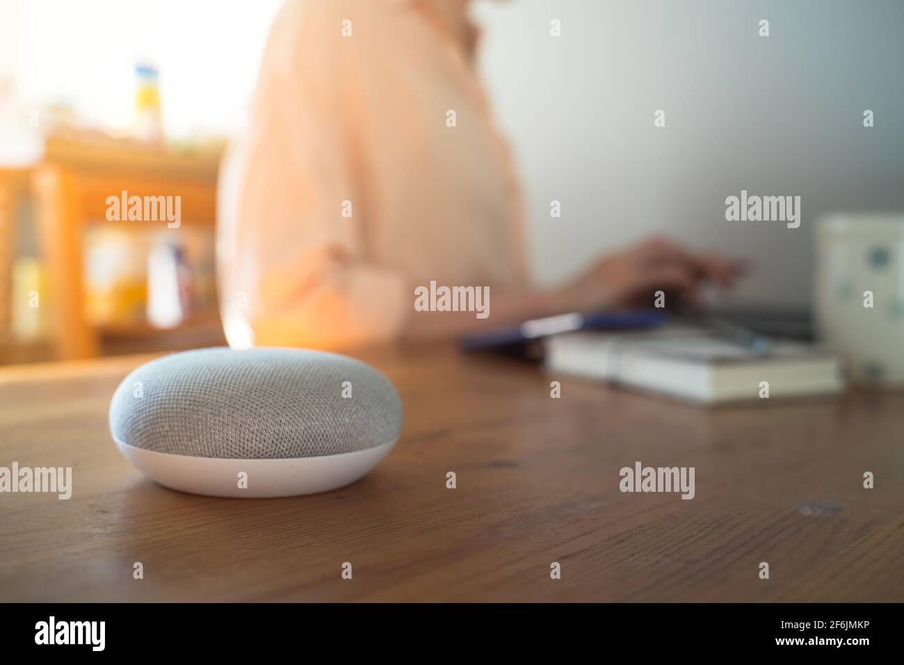 Sprachgesteuerter intelligenter Lautsprecher mit einer Frau im Hintergrund in einer Innenraumumgebung. Stockfoto