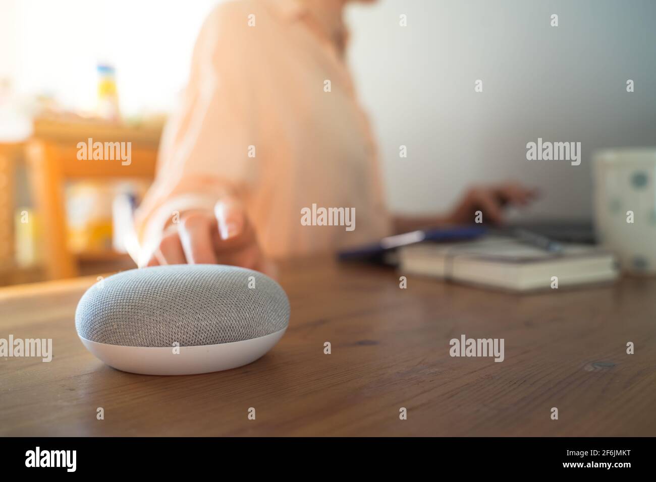 Sprachgesteuerter intelligenter Lautsprecher mit einer Frau im Hintergrund in einer Innenraumumgebung. Stockfoto