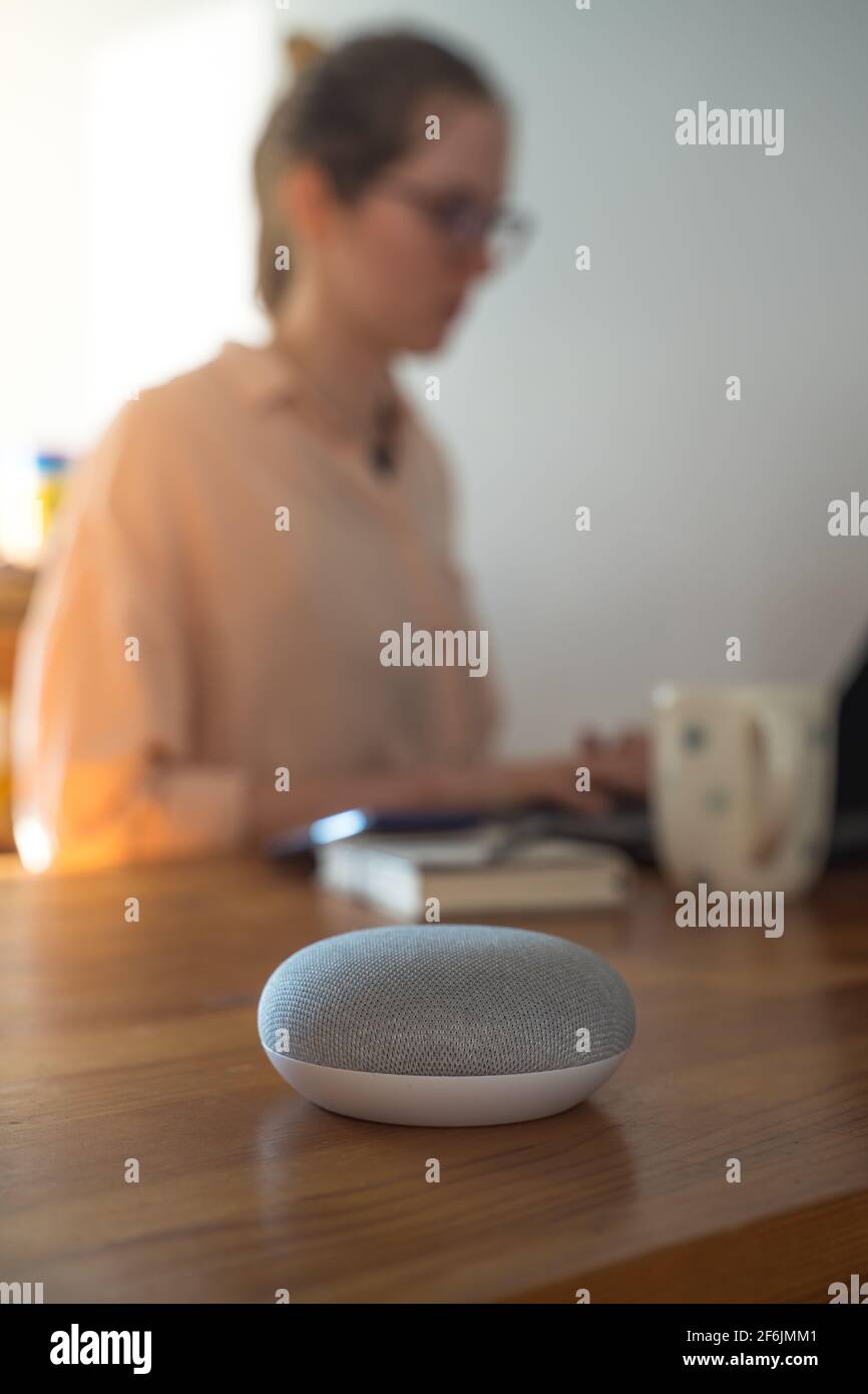 Sprachgesteuerter intelligenter Lautsprecher mit einer Frau im Hintergrund in einer Innenraumumgebung. Stockfoto
