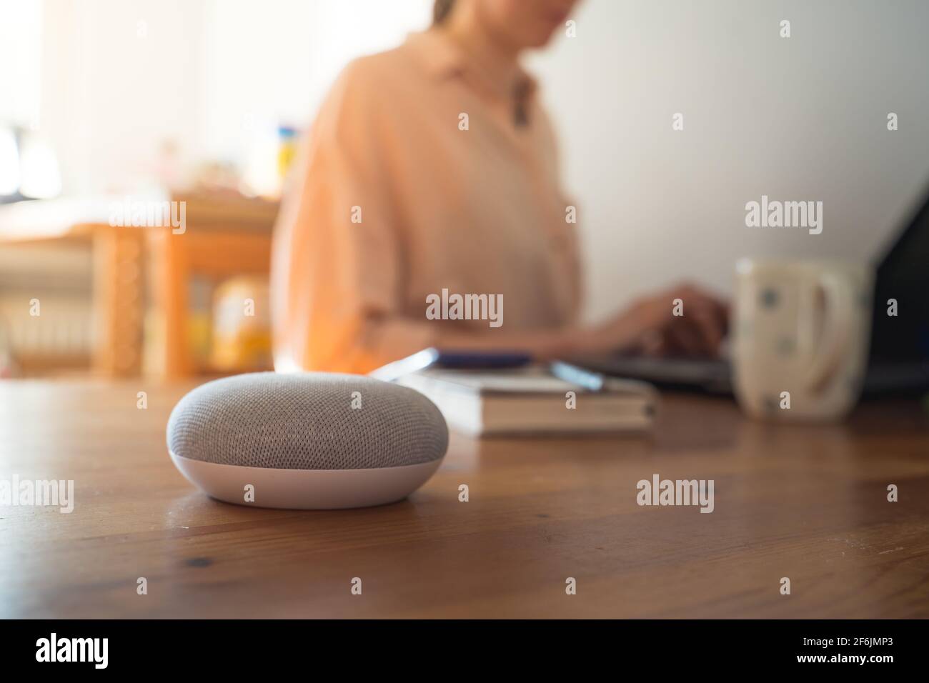 Sprachgesteuerter intelligenter Lautsprecher mit einer Frau im Hintergrund in einer Innenraumumgebung. Stockfoto