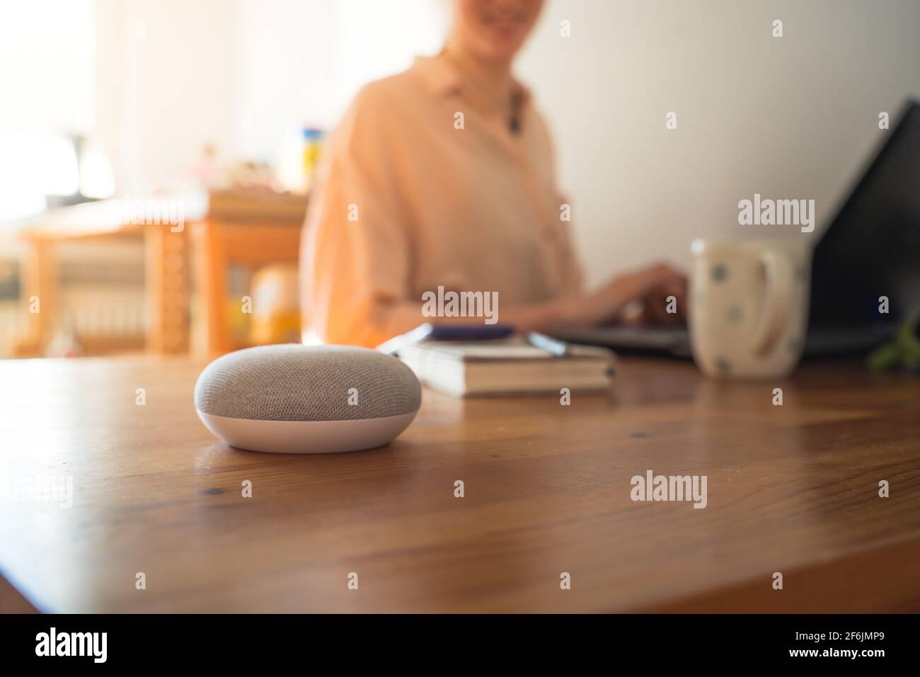 Sprachgesteuerter intelligenter Lautsprecher mit einer Frau im Hintergrund in einer Innenraumumgebung. Stockfoto