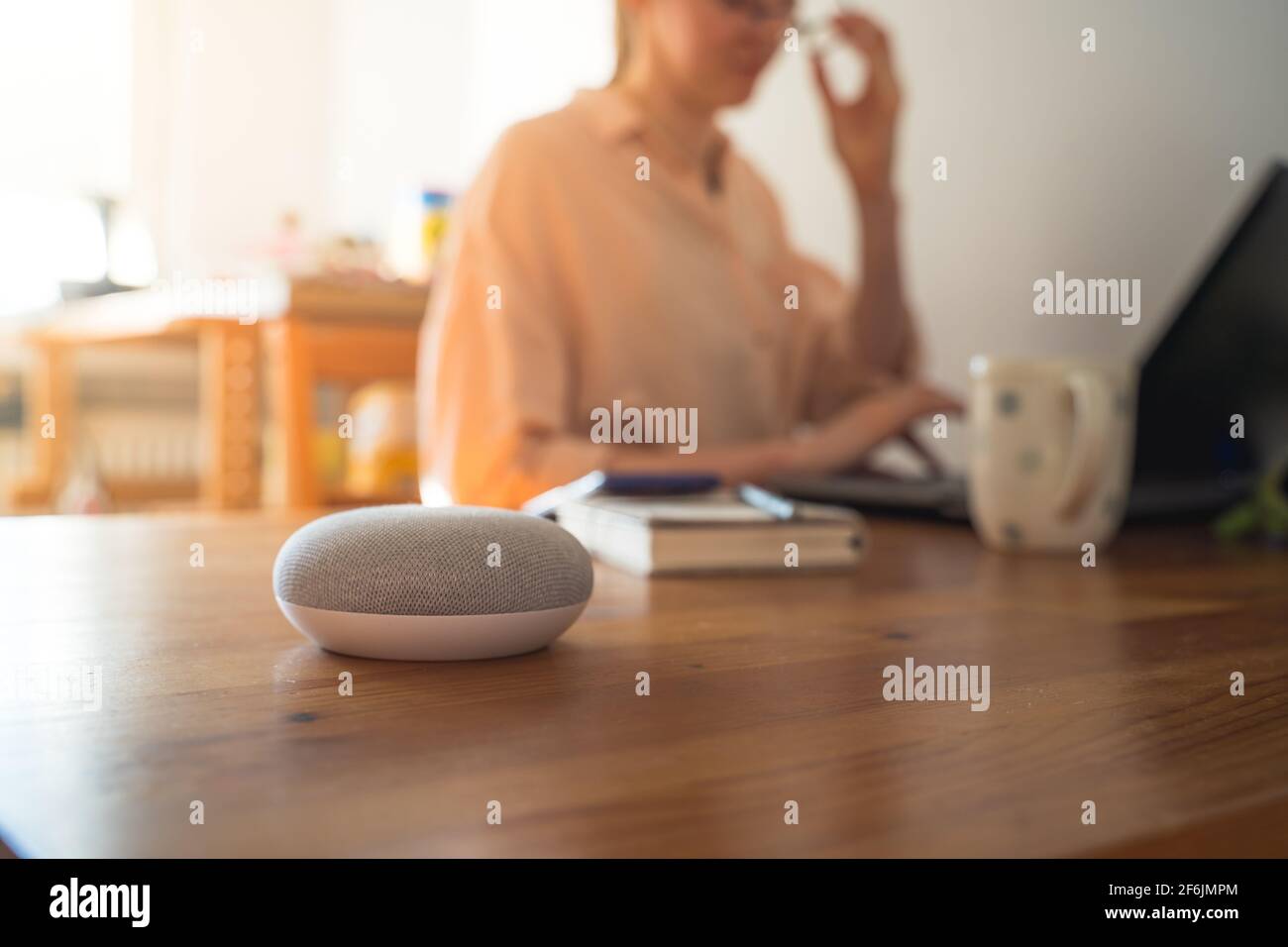 Sprachgesteuerter intelligenter Lautsprecher mit einer Frau im Hintergrund in einer Innenraumumgebung. Stockfoto