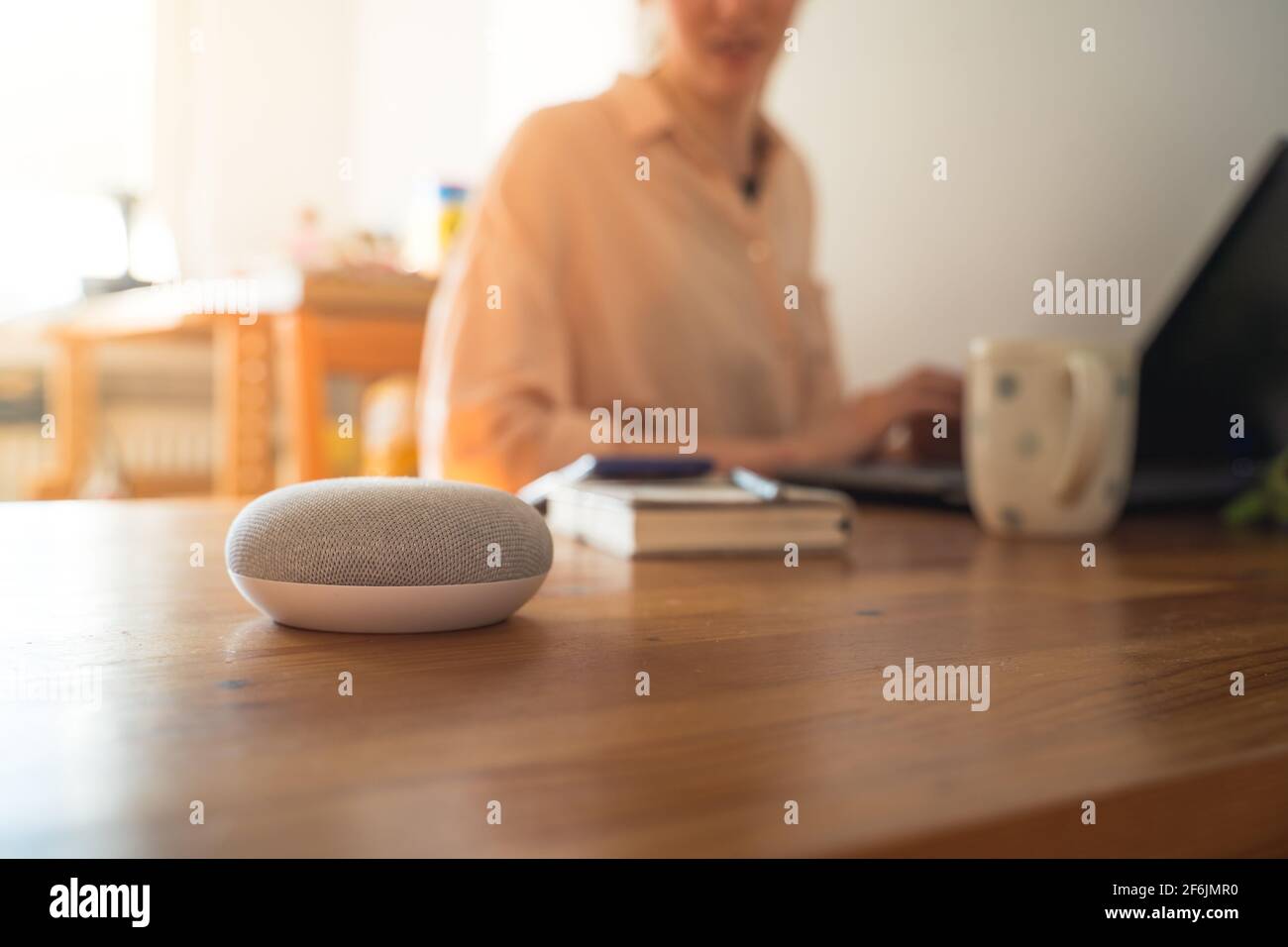 Sprachgesteuerter intelligenter Lautsprecher mit einer Frau im Hintergrund in einer Innenraumumgebung. Stockfoto