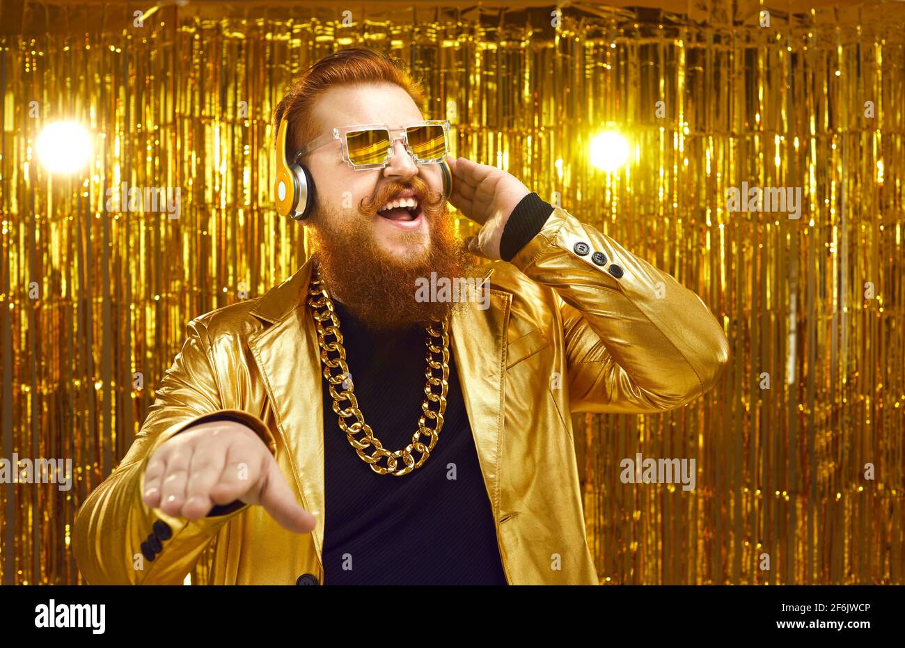 Fröhlicher DJ in glänzender Jacke, Kopfhörern und cooler Sonnenbrille, der Musik auf der Disco-Party spielt Stockfoto