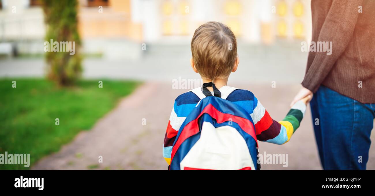 Kind mit Rucksack und mit Mutter vor einem Schulgebäude Stockfoto