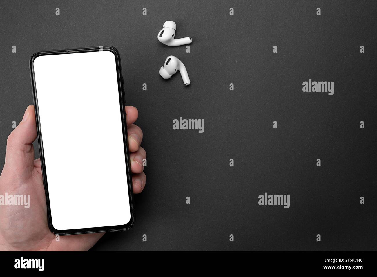 Mockup-Bild. Smartphone mit Handgriff und leerem weißen Bildschirm. Weiße kabellose bluetooth-Kopfhörer oder -Kopfhörer und Smartphone über schwarzem BA Stockfoto