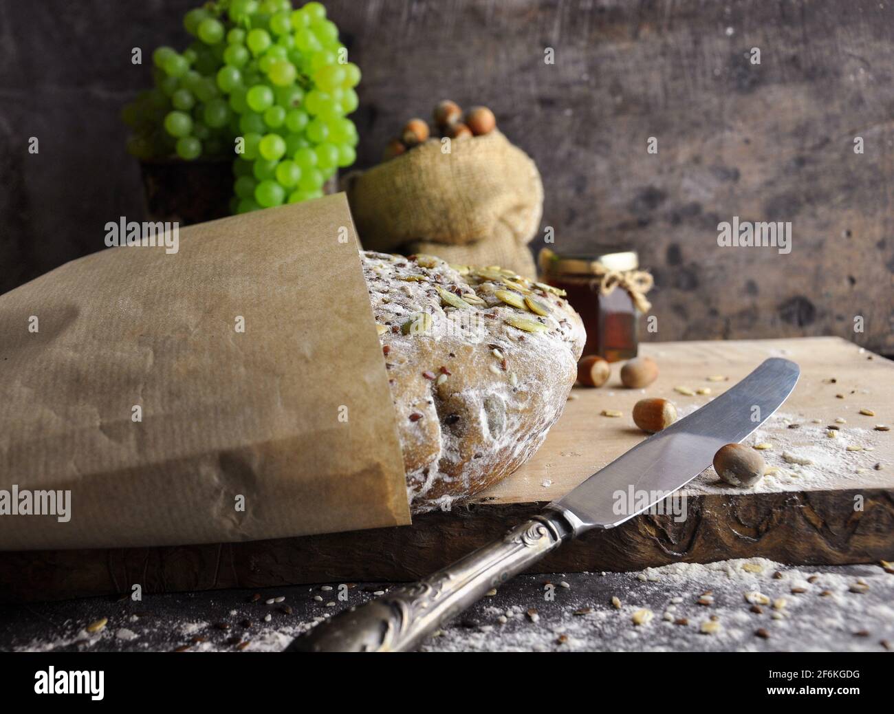 Vollkornbrot in Geschenkpapier. Seitenansicht. Grüne Trauben, Nüsse und Honig im Hintergrund. Provenzalischer Stil. Stockfoto