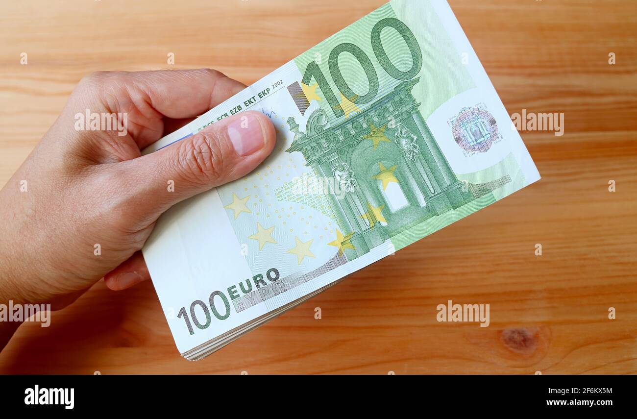 Man's Hand Holding Bundle von 100 EURO Banknoten auf Holz Hintergrund Stockfoto