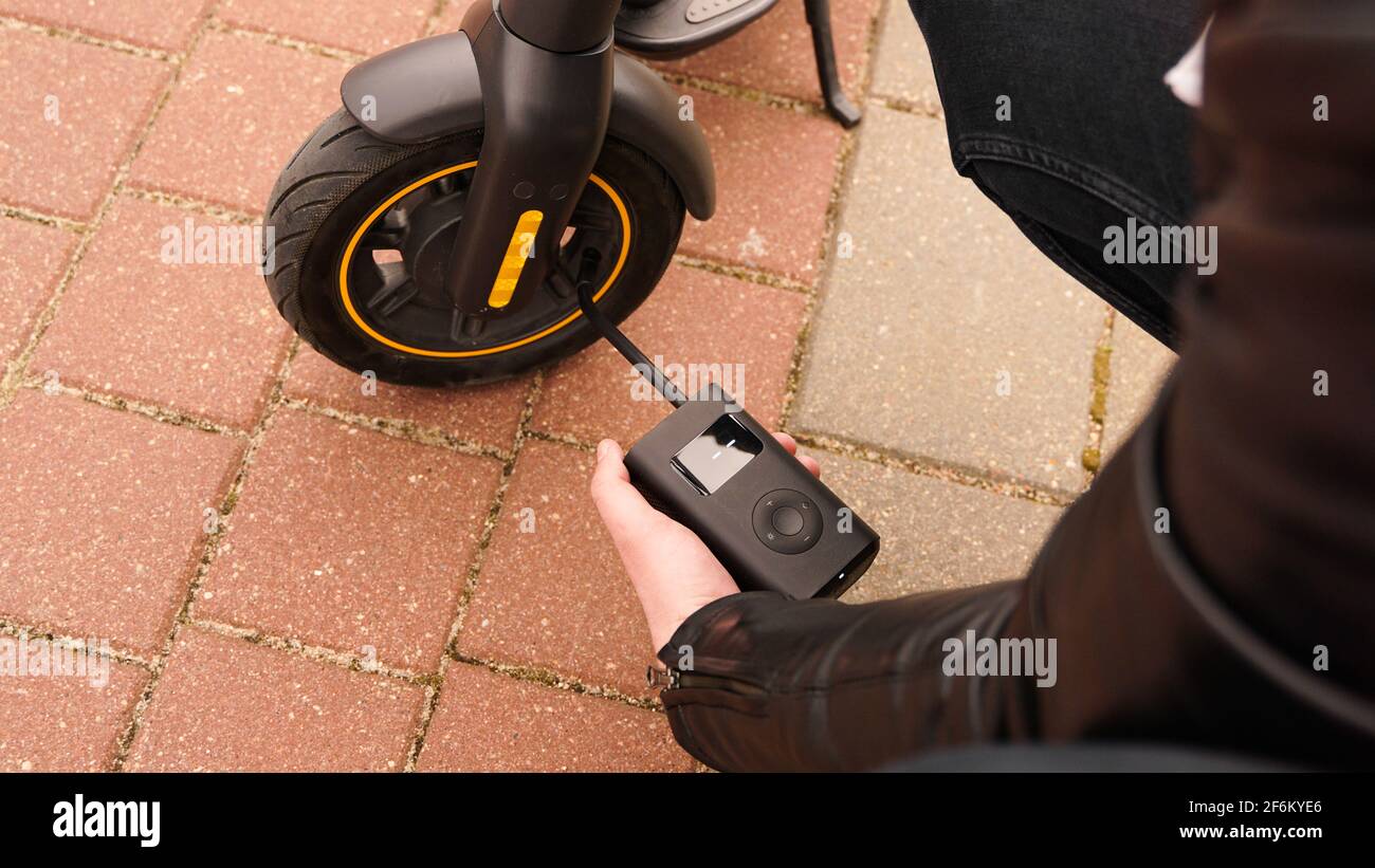 Ein Mann pumpt mit einem speziellen Gerät Luft in das Rad eines Elektrorollers. Stockfoto