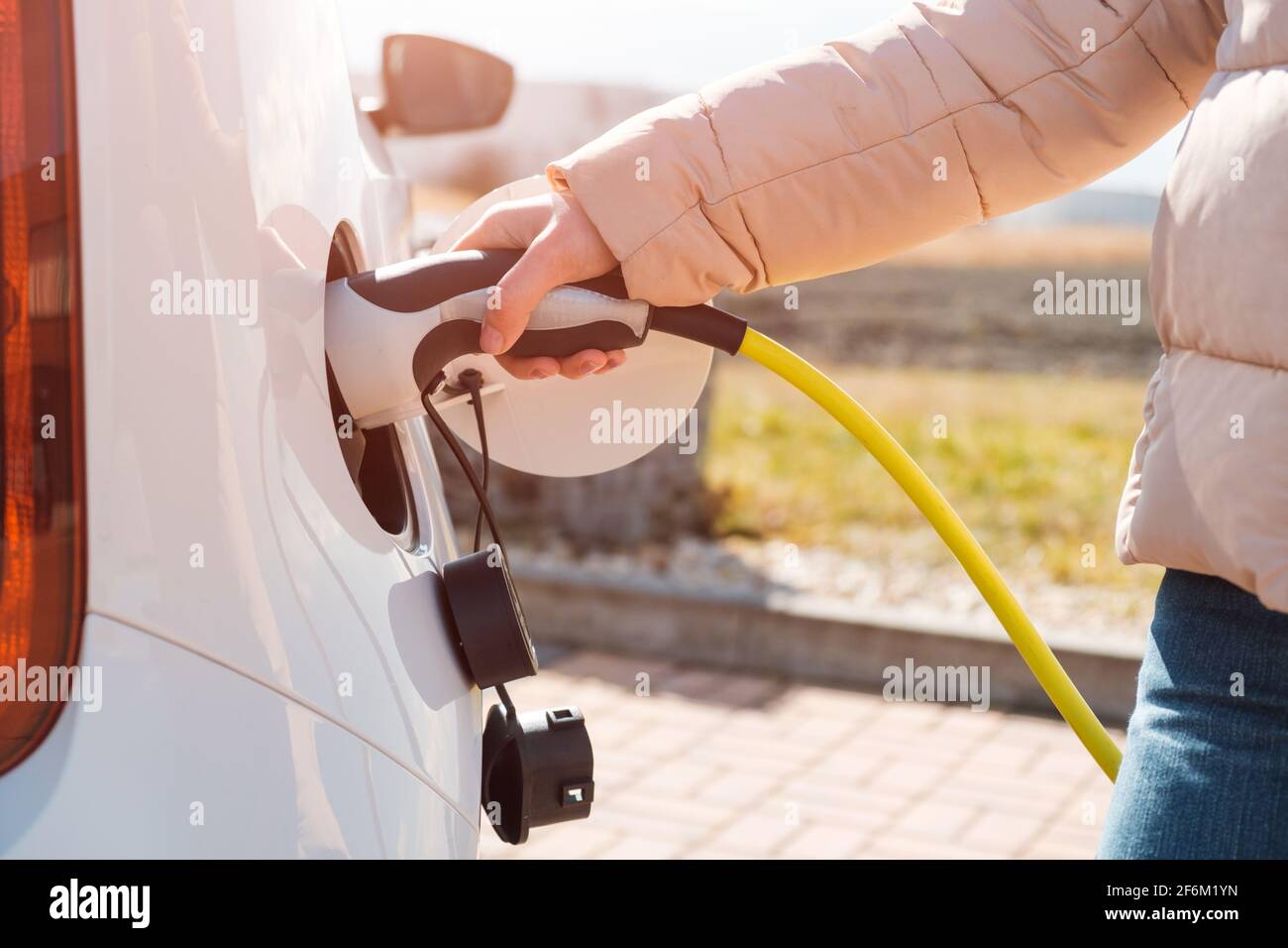 Nahaufnahme Frau, die ein Netzteil an ein elektrisches Gerät anschließt Auto an der Ladestation auf der Straße bei Sonnenlicht Stockfoto