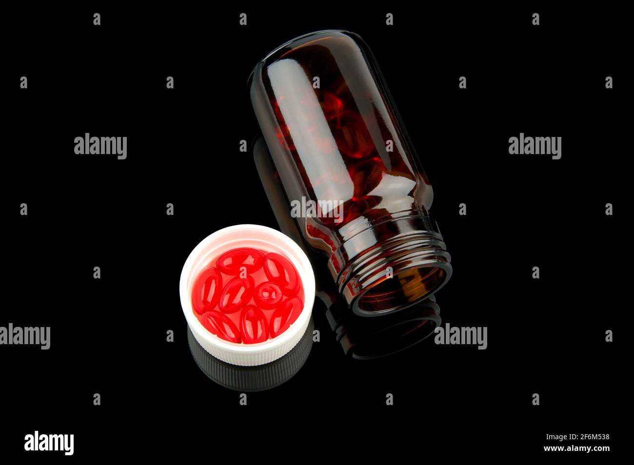 Rote Vitamintabletten im Fläschchen auf glänzendem schwarzem Hintergrund Stockfoto