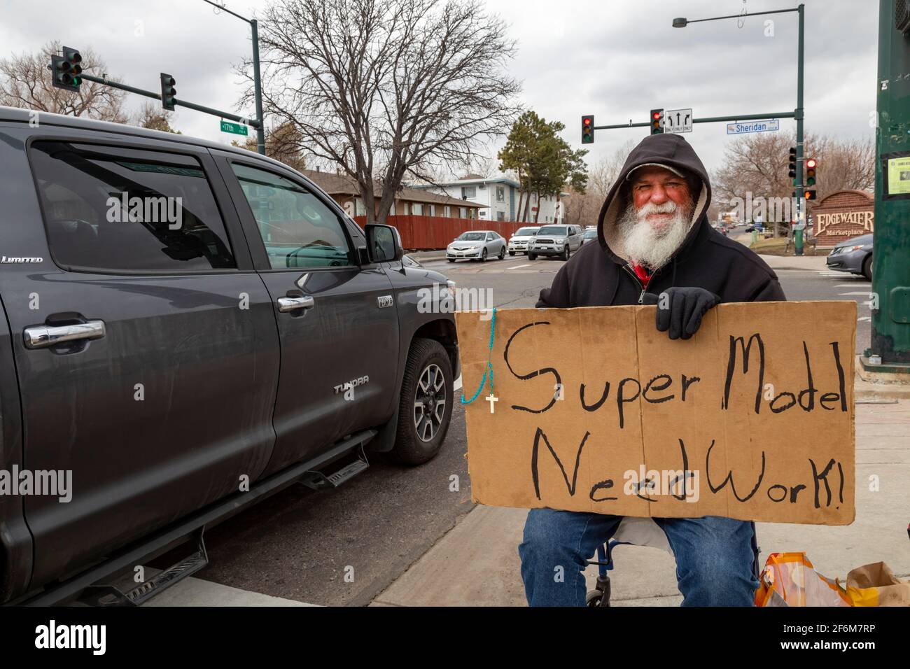 Denver, Colorado - ein scheinbar obdachloser älterer weißer Mann sucht Spenden, während er an einer Straßenecke mit einem Schild sitzt: "Supermodel - braucht Arbeit." Stockfoto