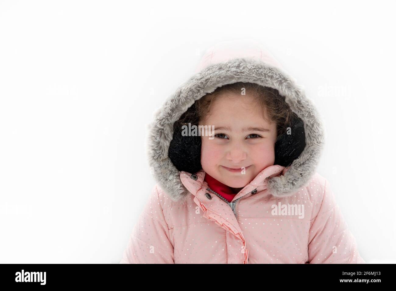 Kleines Mädchen im Alter von 5 Jahren in rosa Winterjacke Posiert vor der Kamera .Hintergrund weißer Schnee Stockfoto