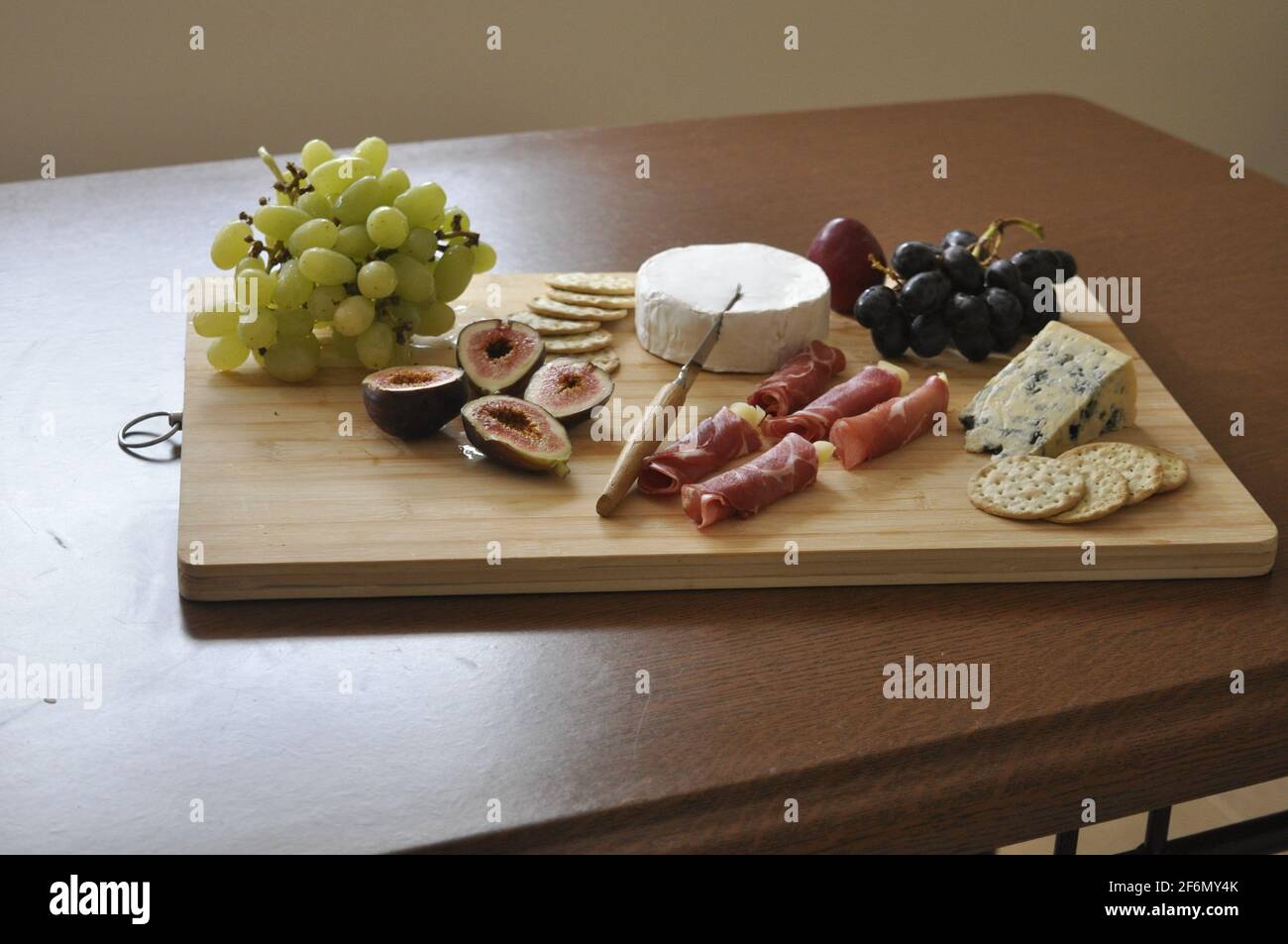 Käseplatte auf einem Holzbrett, Käsemesserfleisch, Blauschimmelkäse, Trauben, Holzschneidebrett, Vorspeise, Messer in den Käse, Fleisch, Essen Stockfoto