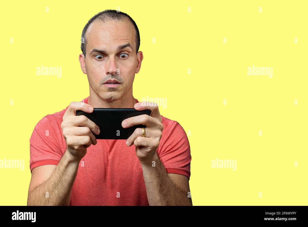 Reifer Mann in lässiger Kleidung, mit weiten Augen und hält das Smartphone waagrecht. Stockfoto