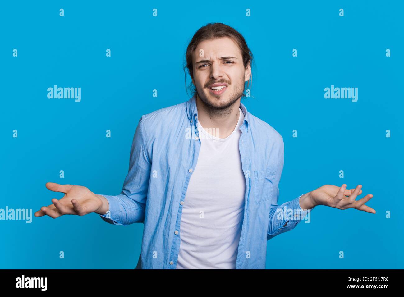 Unentschlossener Mann vergleicht die Dinge auf Handflächen, die nachdenklich sind Kamera auf einer blauen Studiowand Stockfoto