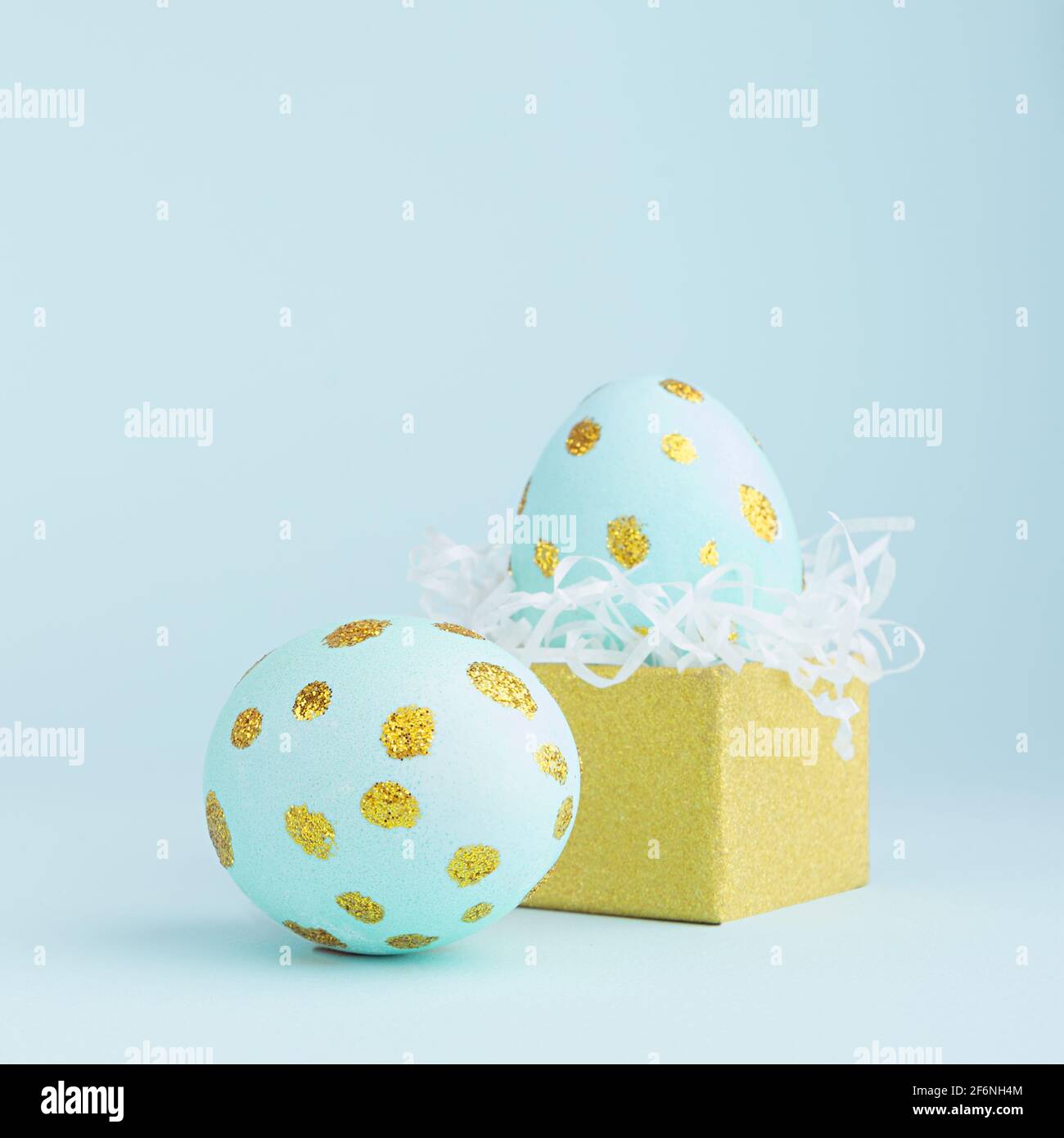 Elegante ostereier mit goldenen Punkten und goldener Geschenkbox auf blauem Hintergrund, quadratisch. Stockfoto