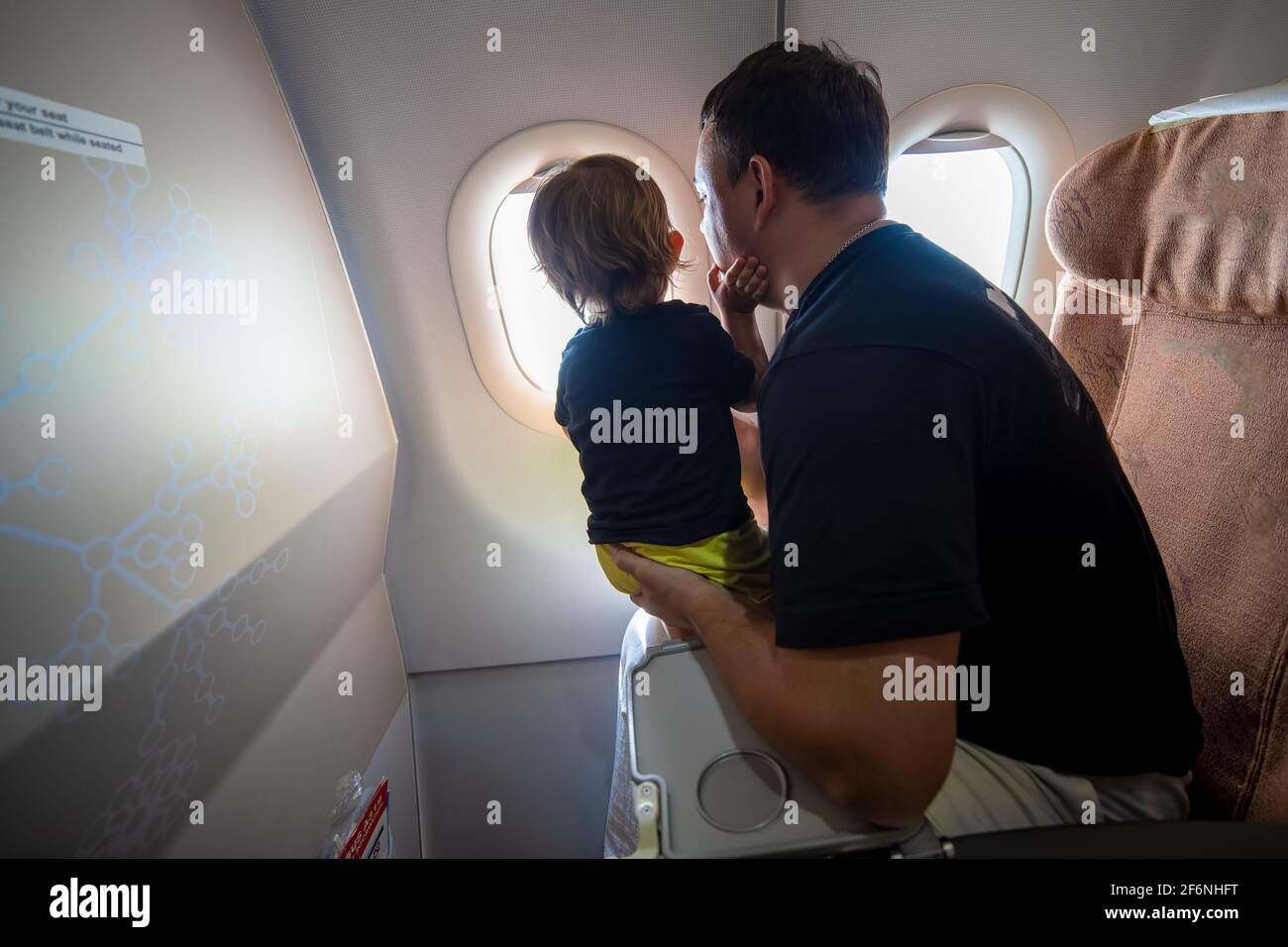 Vater und niedliches Kleinkind sitzen auf einem Flugzeug und schauen in den Himmel durch das Bullauge.. First Flight Konzept, Reisen mit Kindern Stockfoto
