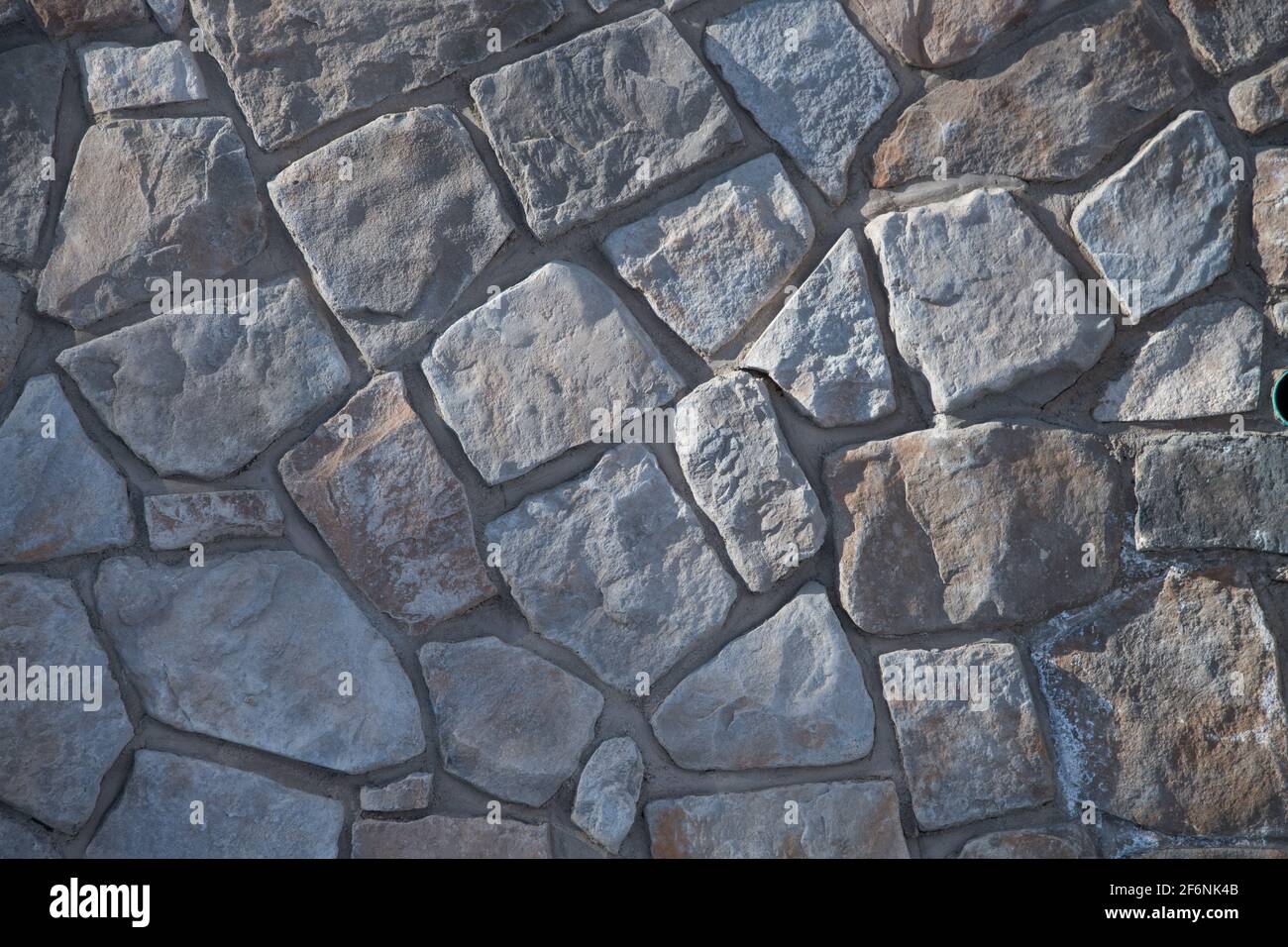 Ungerade geformte Steine oder Felsen passen zusammen wie ein Puzzle, um eine konstruierte Steinmauer Mauerwerk Haus Außenwand Hintergrund Hintergrund oder Tapete zu schaffen Stockfoto