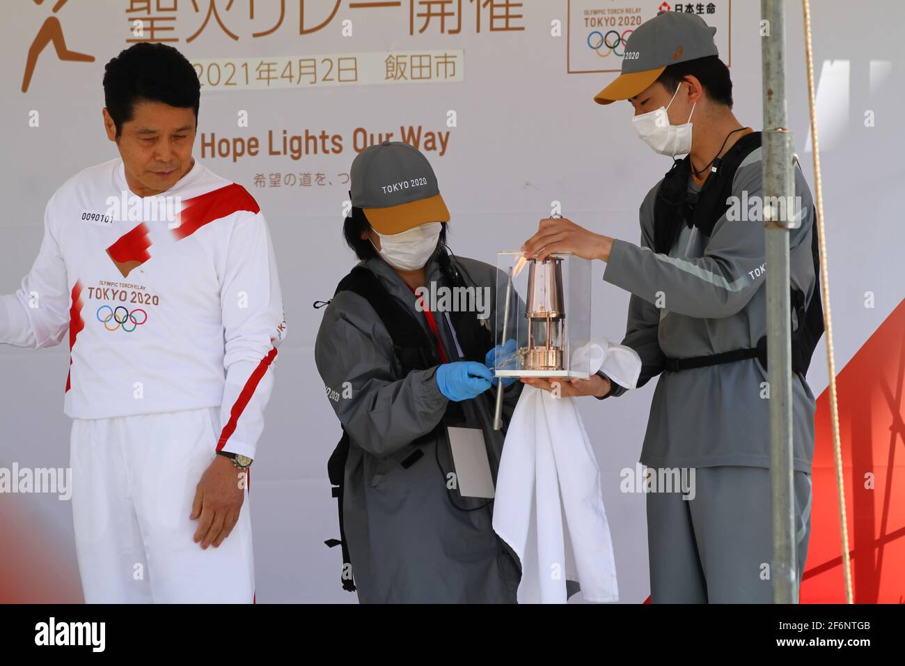 Iida, Japan, 02/04/2021, olympische Fackelveranstaltung in iida. Menschen auf der Bühne, die das Feuer für die Fackel vorbereiten und anzünden. Stockfoto