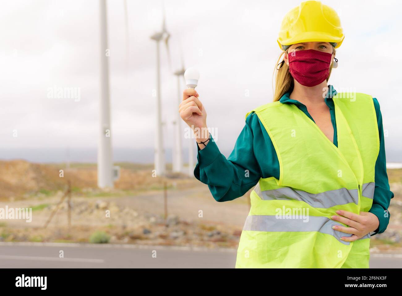 Eine Ingenieurin hält eine Energiesparlampe, im Hintergrund eine Turbine. Erneuerbare Energien, Natur, Strom, Liebe zur Umwelt und zum p Stockfoto