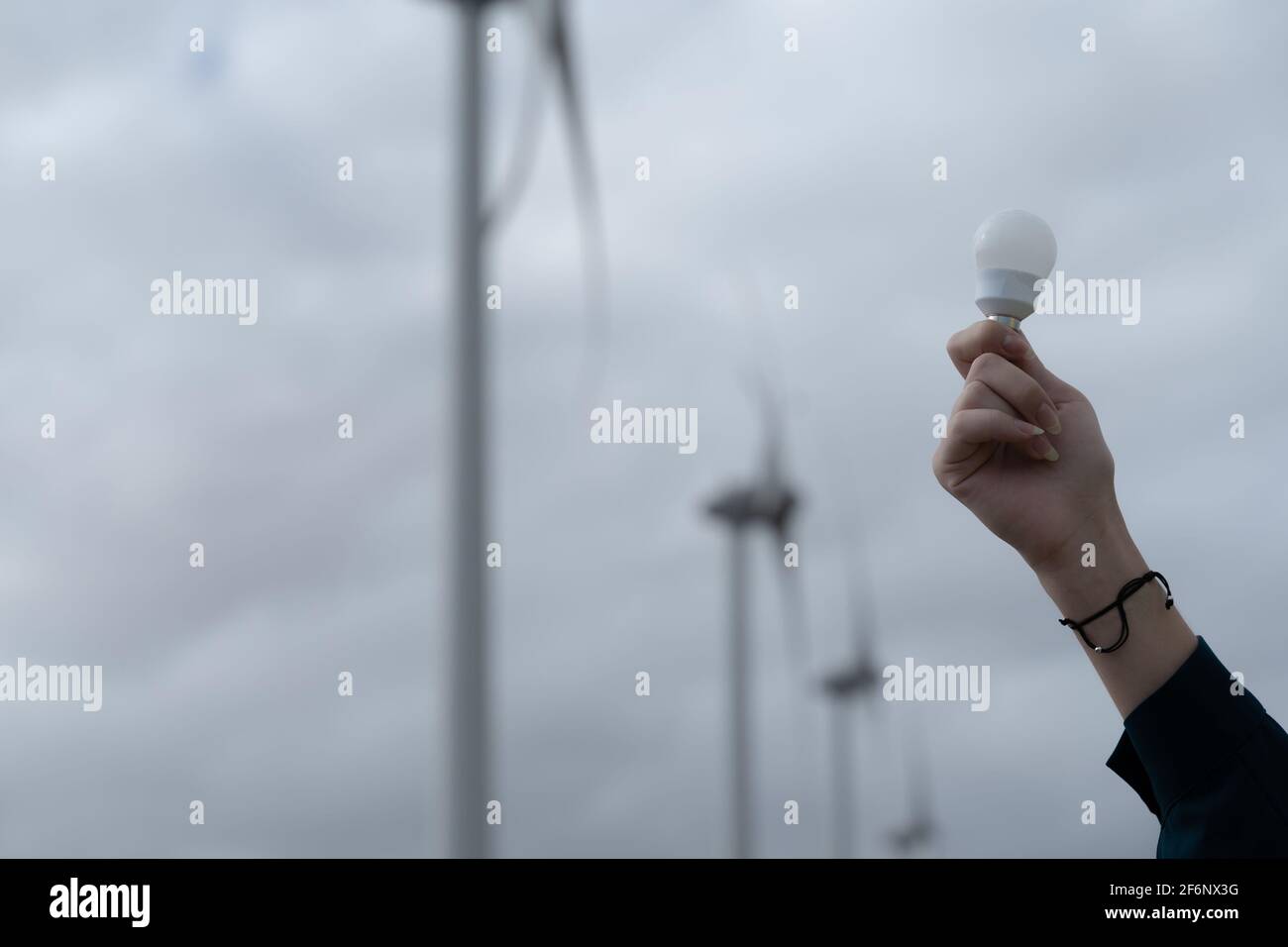 Handportrait der kaukasischen Frau, die eine Energiesparlampe in der Hand hält, im Hintergrund eine Turbine. Erneuerbare Energien, Zukunft und Stromkonzept. Stockfoto