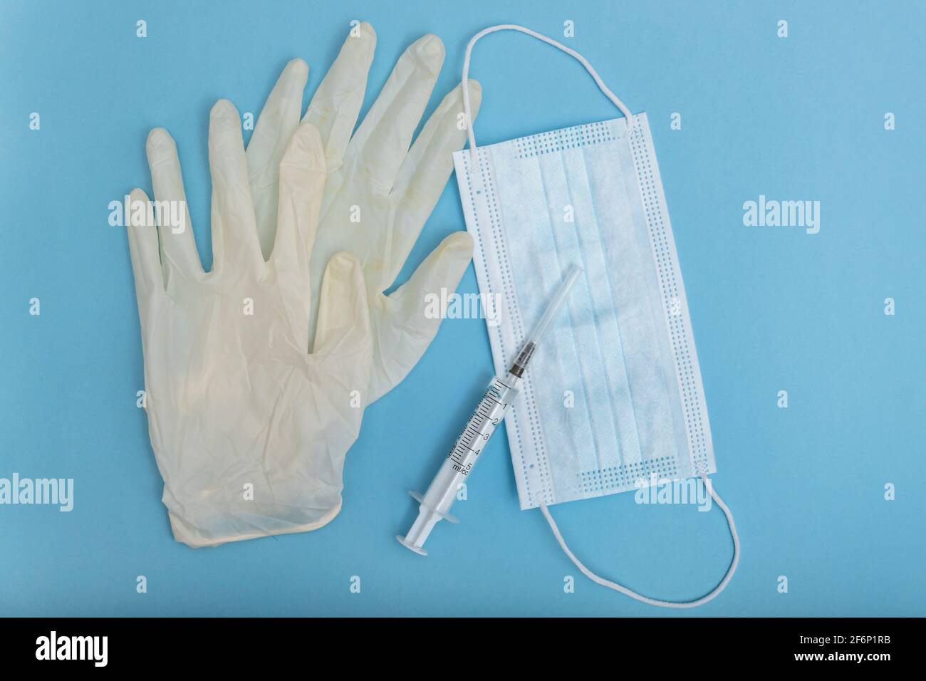 Blaue Einwegmasken und weiße Latexhandschuhe liegen im Hintergrund. Der Hintergrund ist unscharf. Im Vordergrund befindet sich eine Spritze mit einem Impfstoff. Stockfoto