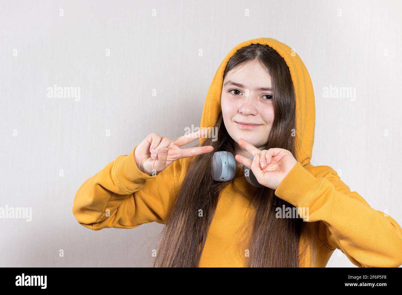 Ein 12-jähriges Teenager-Mädchen in heller Kleidung und einer Kapuze zeigt modische Zeichen mit ihren Fingern. Kopieren Sie den Platz für Text Stockfoto