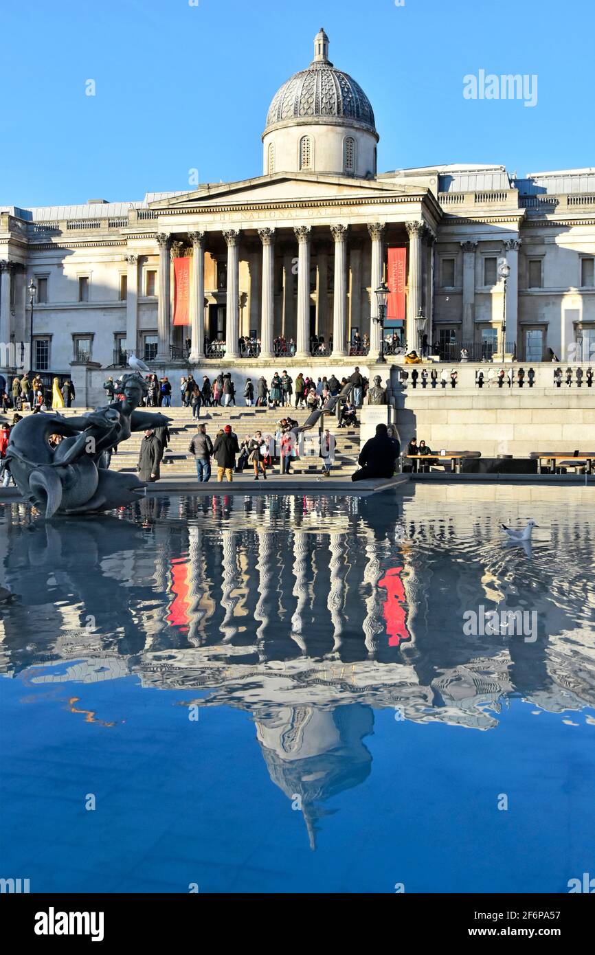 Winteransicht von Touristen & Reflexionen im Trafalgar Square Wasser Springbrunnenpool im berühmten historischen Kunstmuseum der National Gallery London, England, Großbritannien Stockfoto