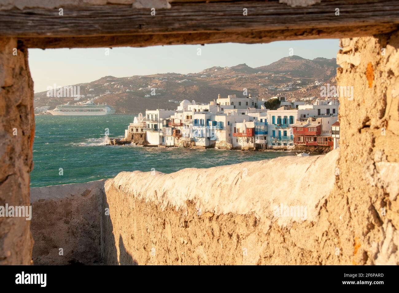 Uferpromenade des Dorfes Mykonos in Griechenland durch ein Natursteinfenster. Im Hintergrund die Ägäis und die Küste der Insel Stockfoto