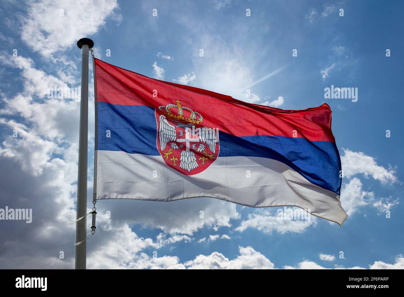 Flagge Serbiens, nationales Symbol der Republik Serbien auf einem Fahnenmast, der gegen den blau bewölkten Himmel winkt Stockfoto
