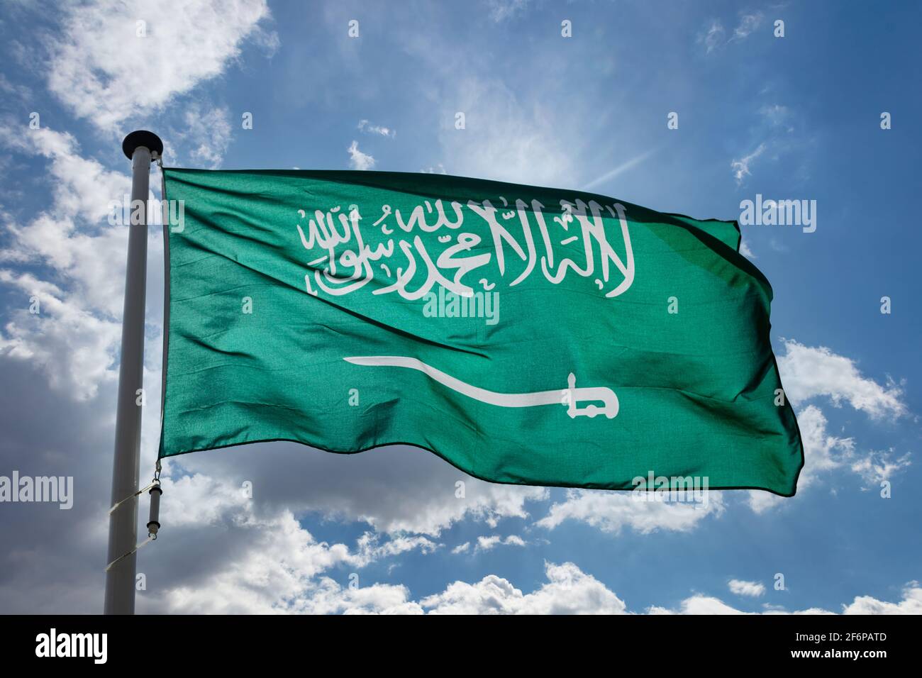Flagge Saudi-Arabiens, nationales Symbol des Königreichs Saudi-Arabien auf einem Fahnenmast, der gegen den blau bewölkten Himmel winkt Stockfoto