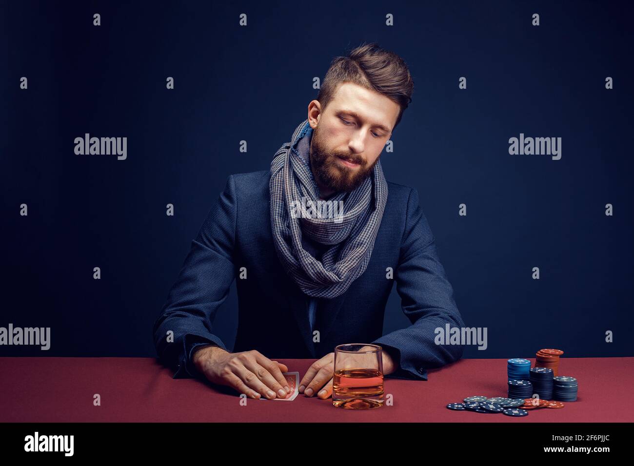 Stilvoller bärtiger Mann, der im dunklen Kasino spielt, Zigarre raucht, Whiskey trinkt Stockfoto