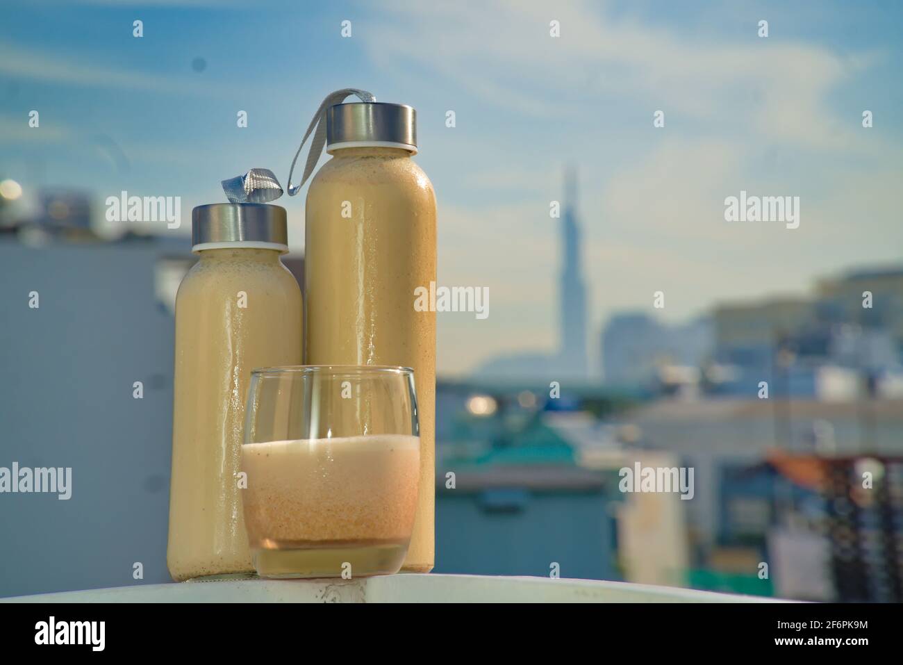 Wiederverwendbare Flaschen und ein Glas cremiges Getränk auf einem Dach mit urbaner Skyline-Kulisse. Ein modernes Lifestyle-Image, das Nachhaltigkeit, Gesundheit fördert Stockfoto