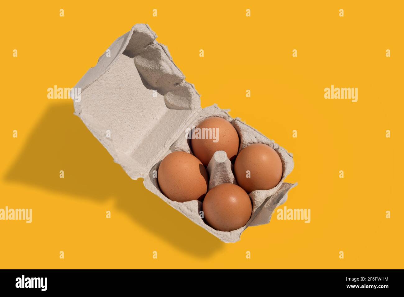 Eierkarton mit Eiern, vier Hühnereier in Pappeiablage aus recyceltem Papier, isoliert auf gelbem Hintergrund Stockfoto