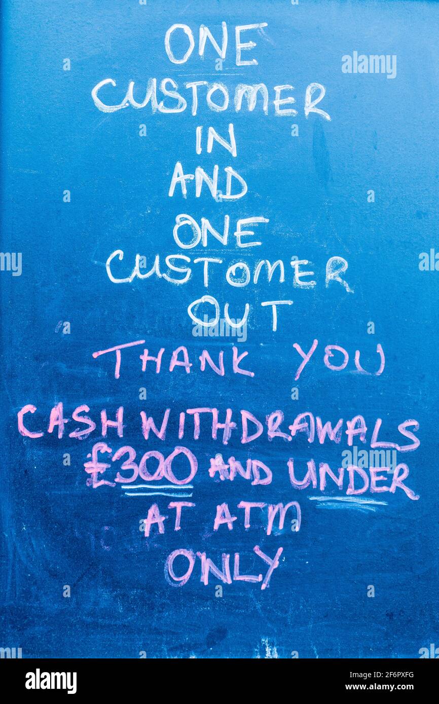 Kreidezeichen auf blauem Brett außerhalb der Bank, das Kundenbesuche aufgrund der englischen COVID-Pandemiesperre auf einen nach dem anderen begrenzt. Stockfoto