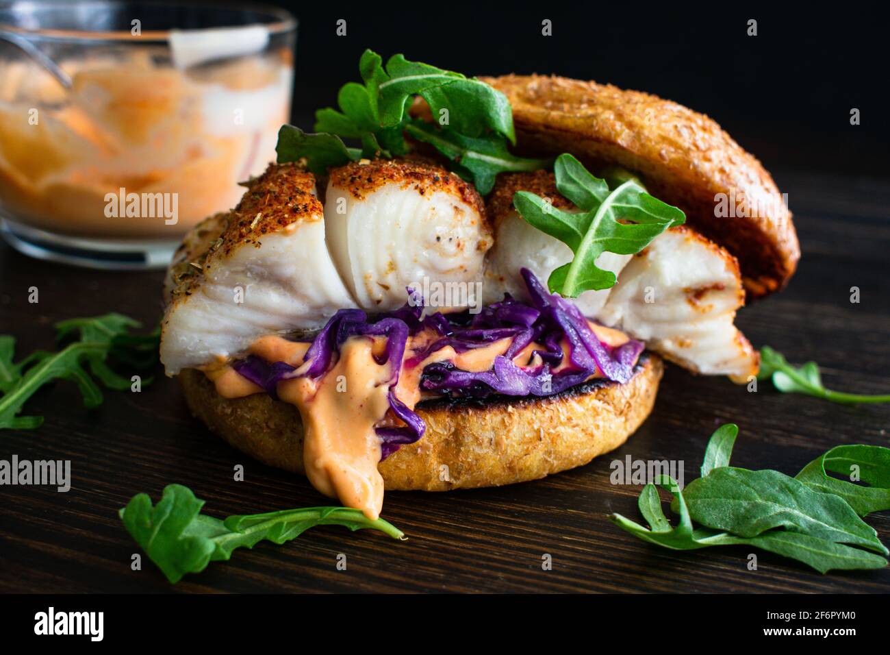 Brockened Fish Burger und Sriracha Mayo: Ein Fischsandwich aus Heilbutt mit Rotkohl und Rucola auf einem Vollkornbrötchen Stockfoto
