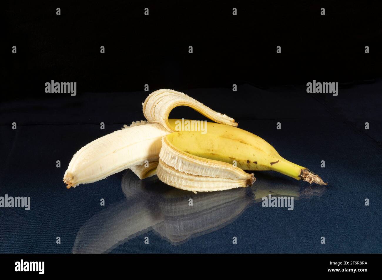 Eine reife Banane auf einem Glastisch mit Spiegelung. Essen auf schwarzem Hintergrund Stockfoto