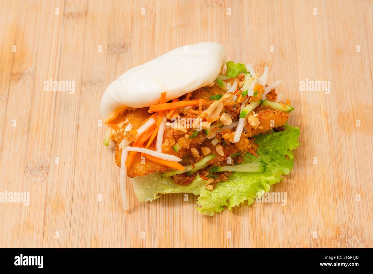 Köstliches gedämpftes bao-Brötchen auf Holztisch mit gebratenem Huhn und frischem Gemüse - Salat, Karotten und gerösteten Erdnüssen. Beliebtes Street Food Stockfoto