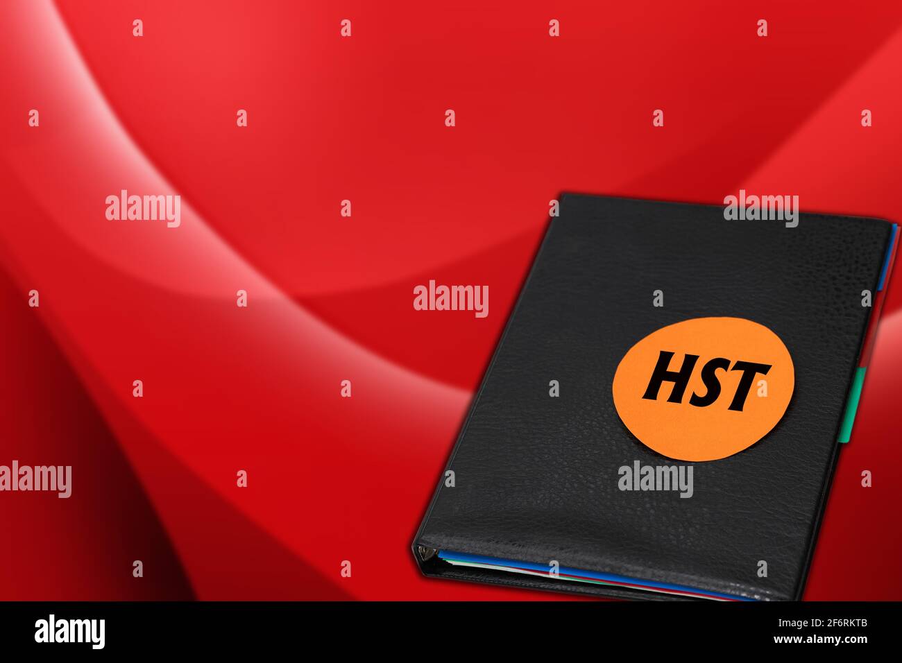 Harmonisierte Umsatzsteuer-HST-Notiz auf orangefarbenem Aufkleber Schwarzer Ordner auf rotem Hintergrund Stockfoto