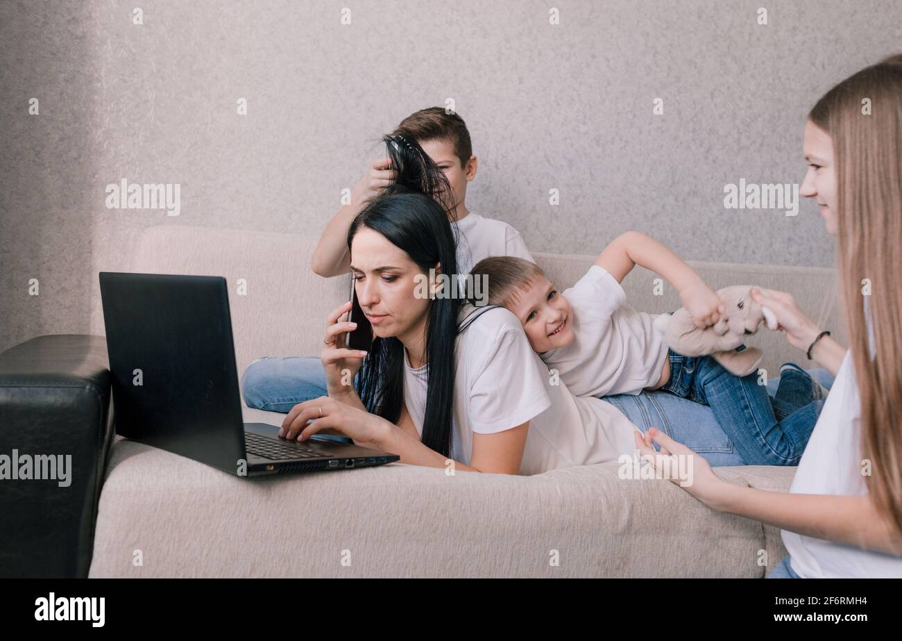 Aktive Kinder frönen, stören und ablenken ihre Mutter, während sie zu Hause auf einem Laptop arbeiten Stockfoto