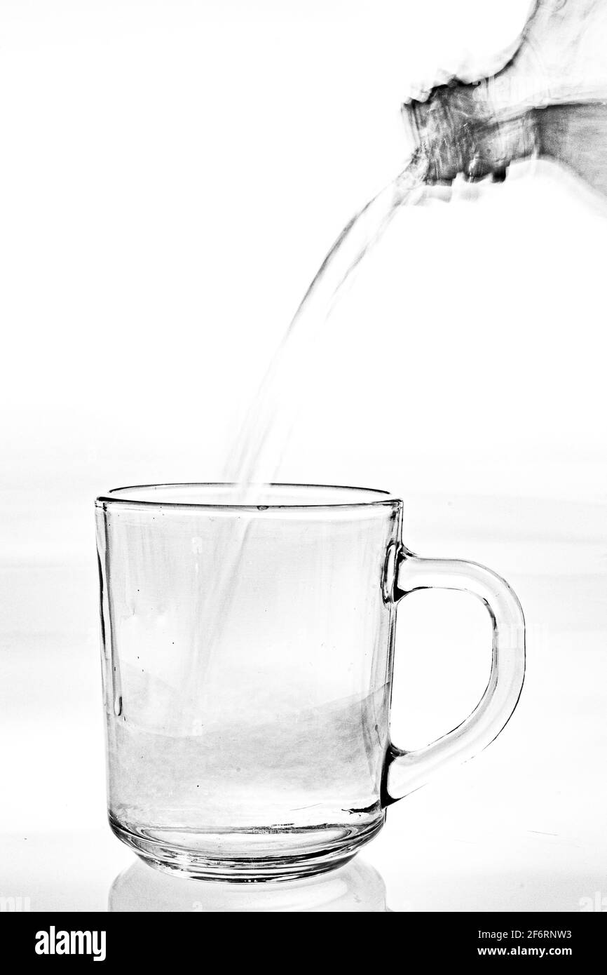 Wasser aus einer Flasche in ein Glas gegossen. Durst mit Trinkwasser löschen. Heller Hintergrund. Stockfoto