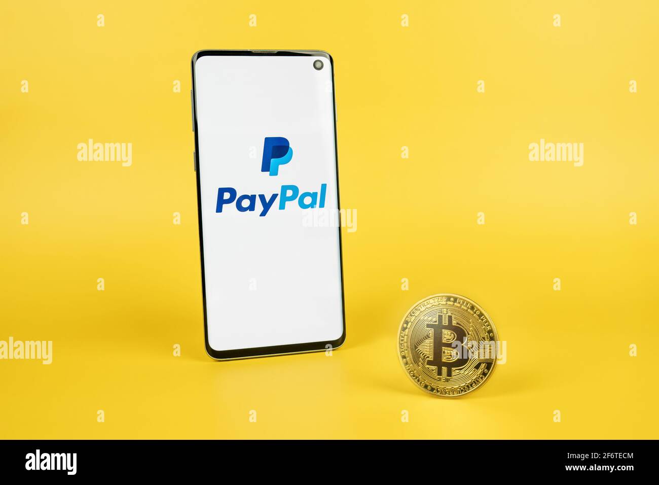 PayPal-Logo auf dem Telefonbildschirm mit Bitcoin Kryptowährung Münze auf gelbem Hintergrund. Kasse mit Crypto, neues Zahlungsoptionen-Konzept Stockfoto