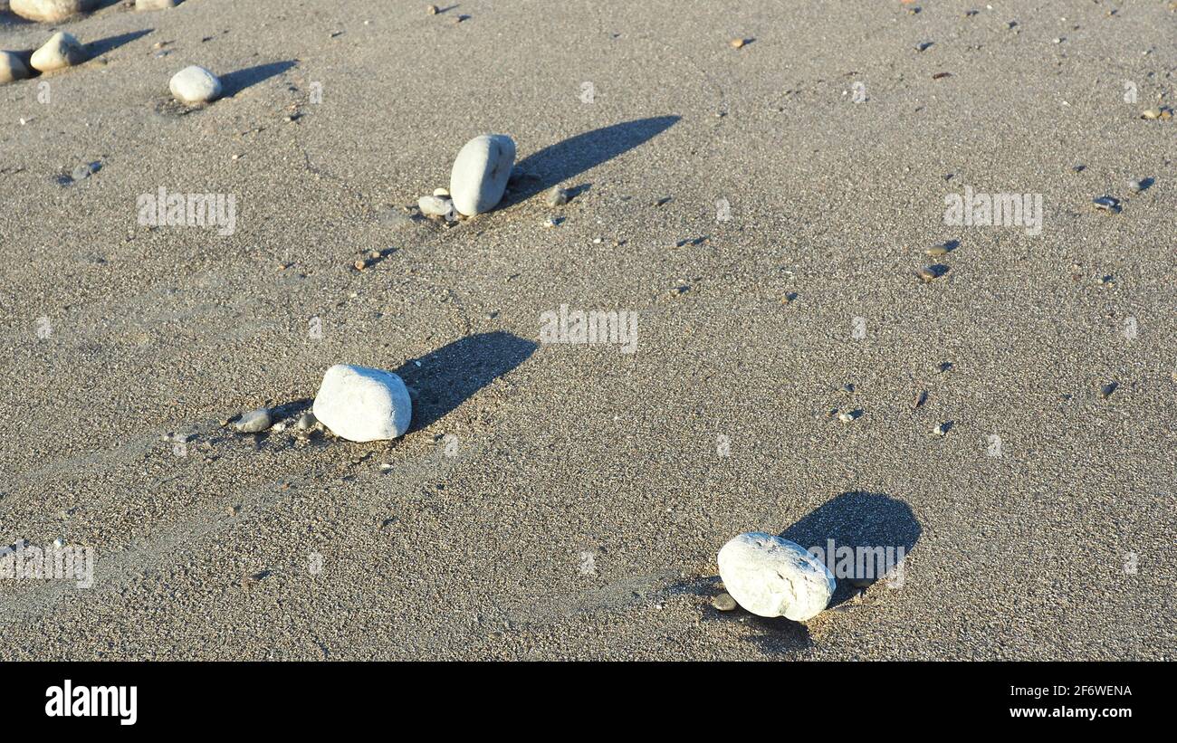 Verstreute Steine am Strand von Te Horo werfen am späten Nachmittag Schatten an der Westküste von Neuseeland Stockfoto